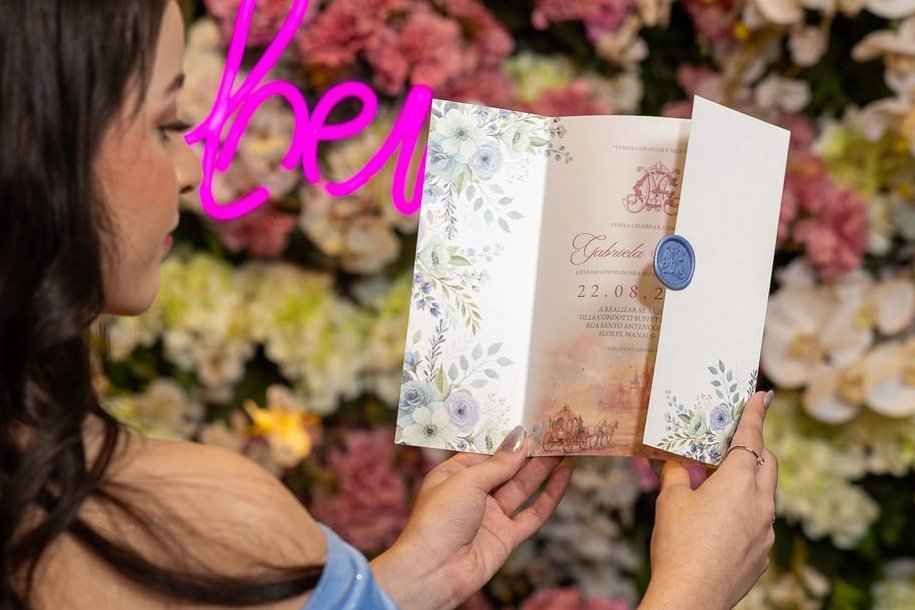Convidada lendo convite personalizado em frente a painel de flores, identidade de evento